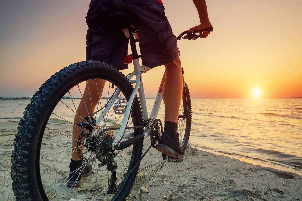 Man on mountain bike watches sunset over the ocean